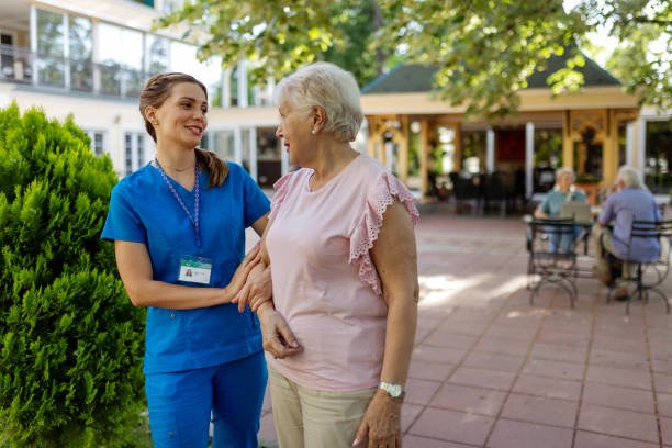 Senior Woman and Young Female Caregiver Communicating Outdoors at Nursing Home.